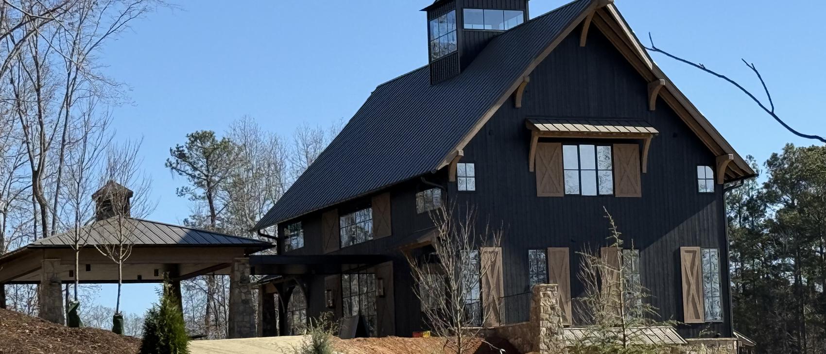 Black barn home clad in charred wood with standing seam roof, cupola, and heavy timber bracing