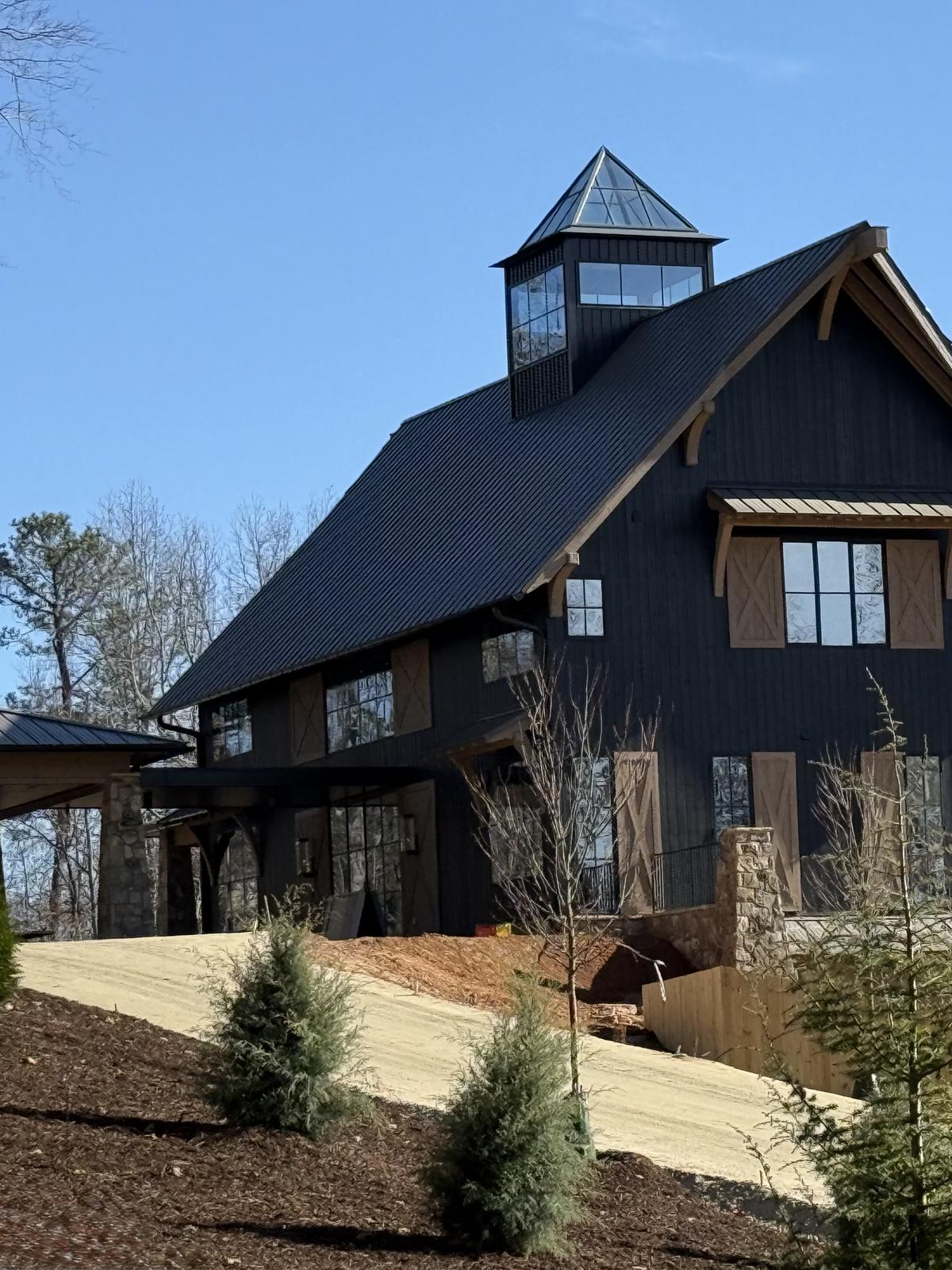 Black barn home with cupola on a wooded hillside