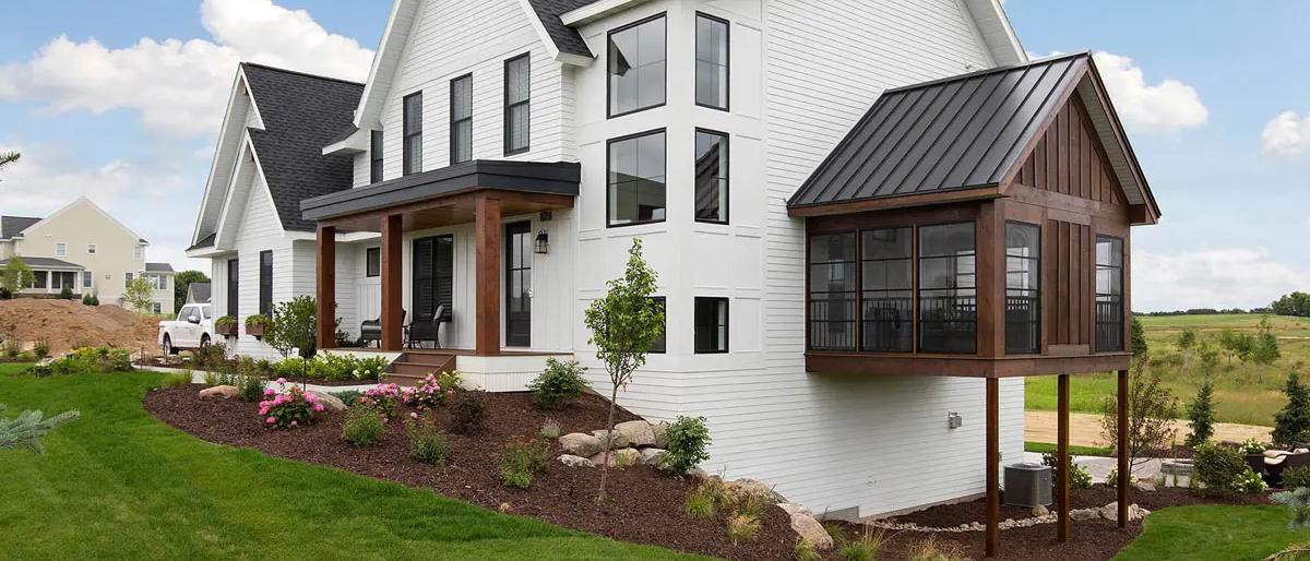 White lap siding farmhouse with standing seam porch roof, black windows, and stained timber columns