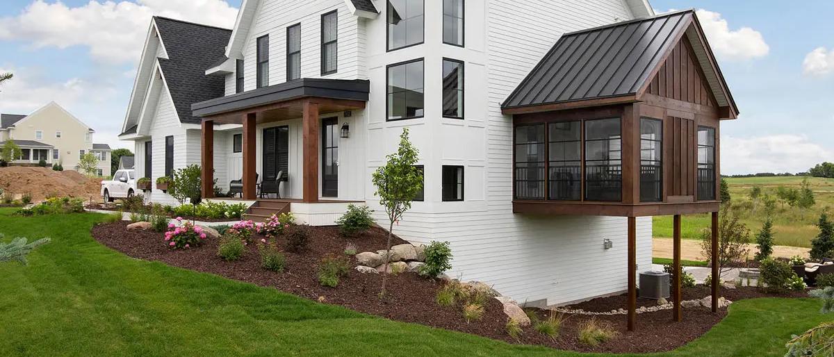 Farmhouse with a screened porch addition under a standing seam roof with stained timber posts