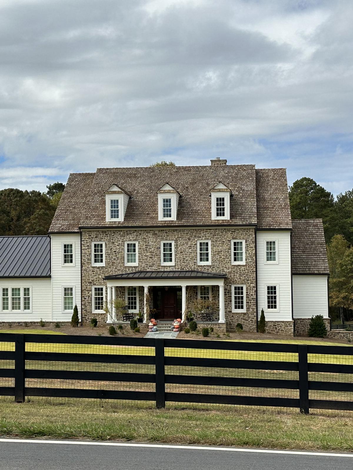 Stone and siding country home behind a black board fence